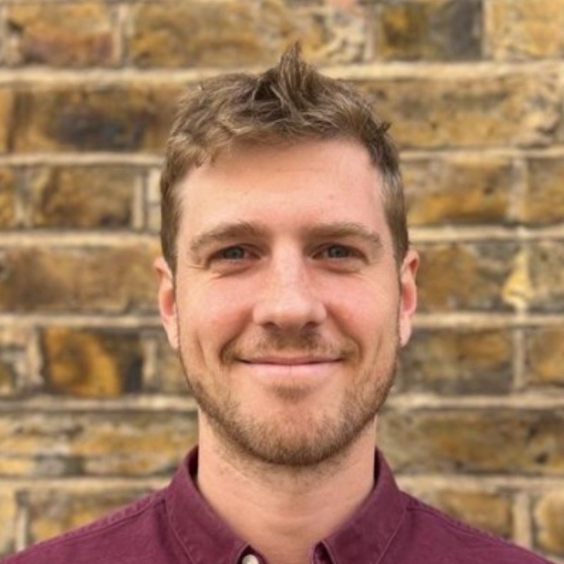 Smiling person in front of a brick wall.
